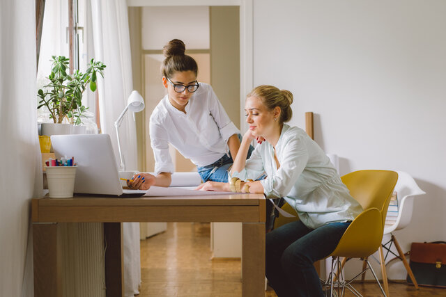 Zwei junge Frauen arbeiten gemeinsam an einem Dokument auf einem Arbeitstisch.