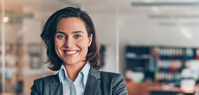 Eine Frau im Anzug steht vor einem modernen Büro.